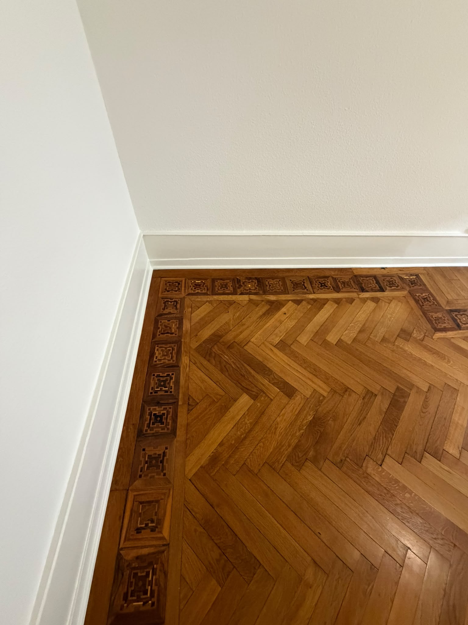 Angle de pièce après peinture : murs blancs mats, plinthes laquées, parquet à frise marquetée
