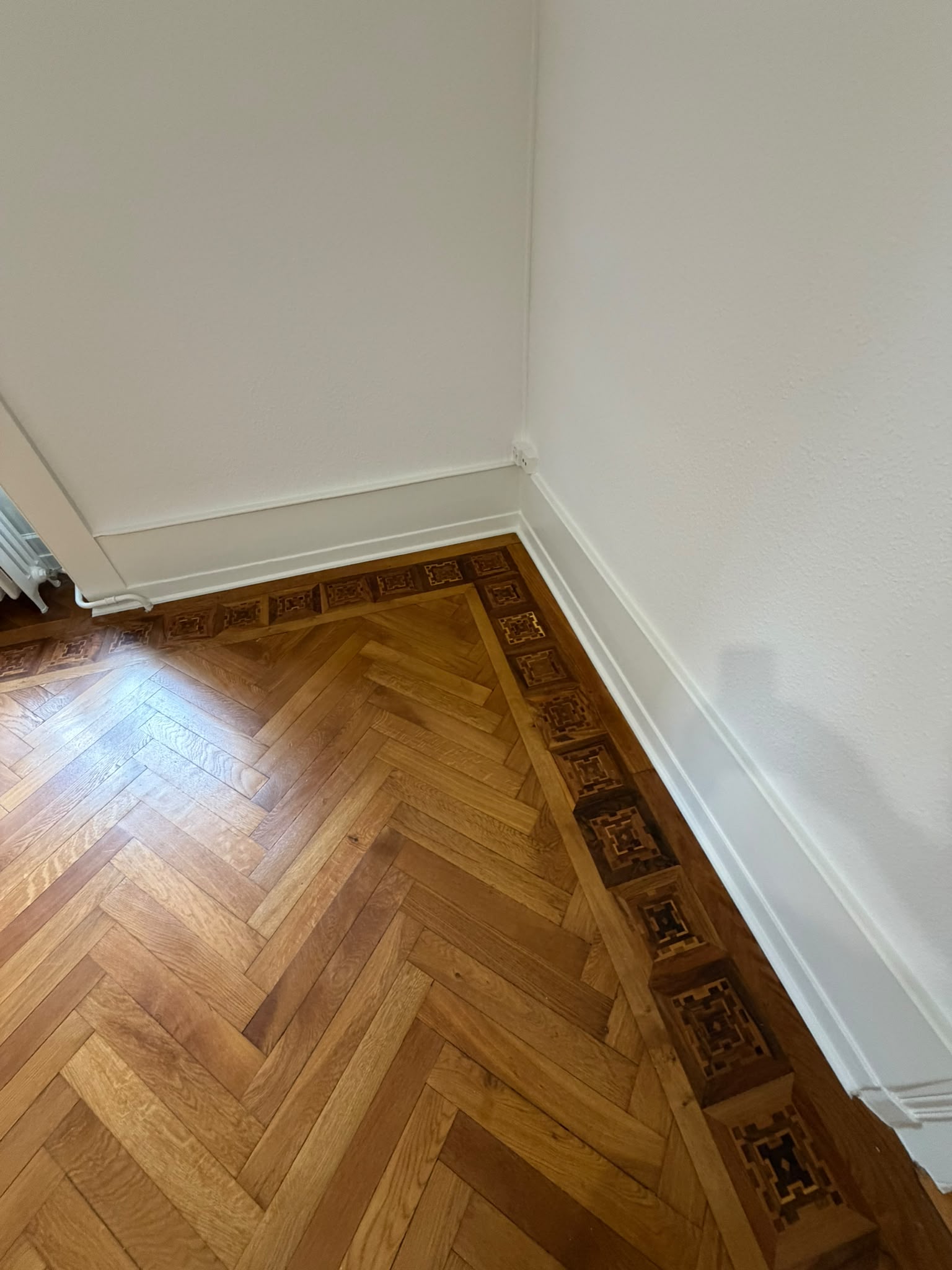 Murs et plinthes repeints en blanc dans une pièce avec parquet à bâtons rompus et frise