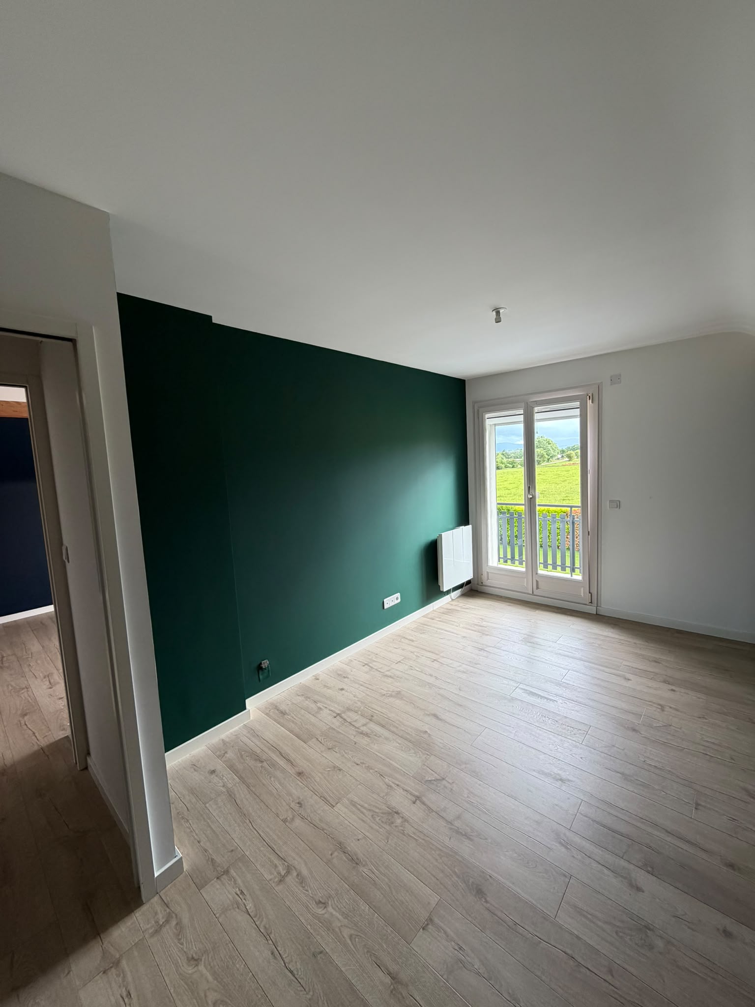 Chambre avec un mur d’accent peint en vert sapin et les autres murs en blanc, parquet clair