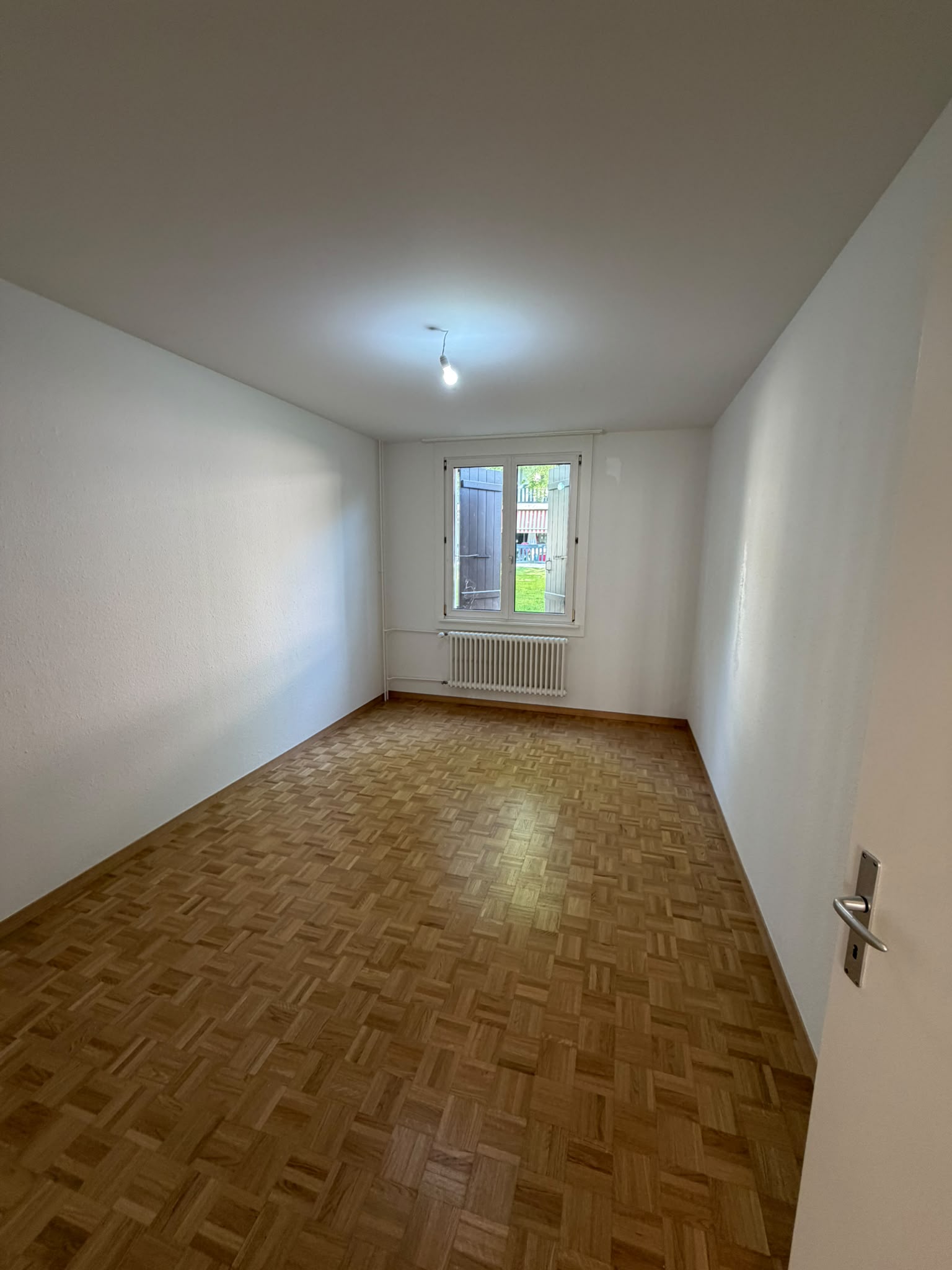 Chambre aux murs et plafond blancs après peinture, parquet mosaïque, fenêtre sur jardin