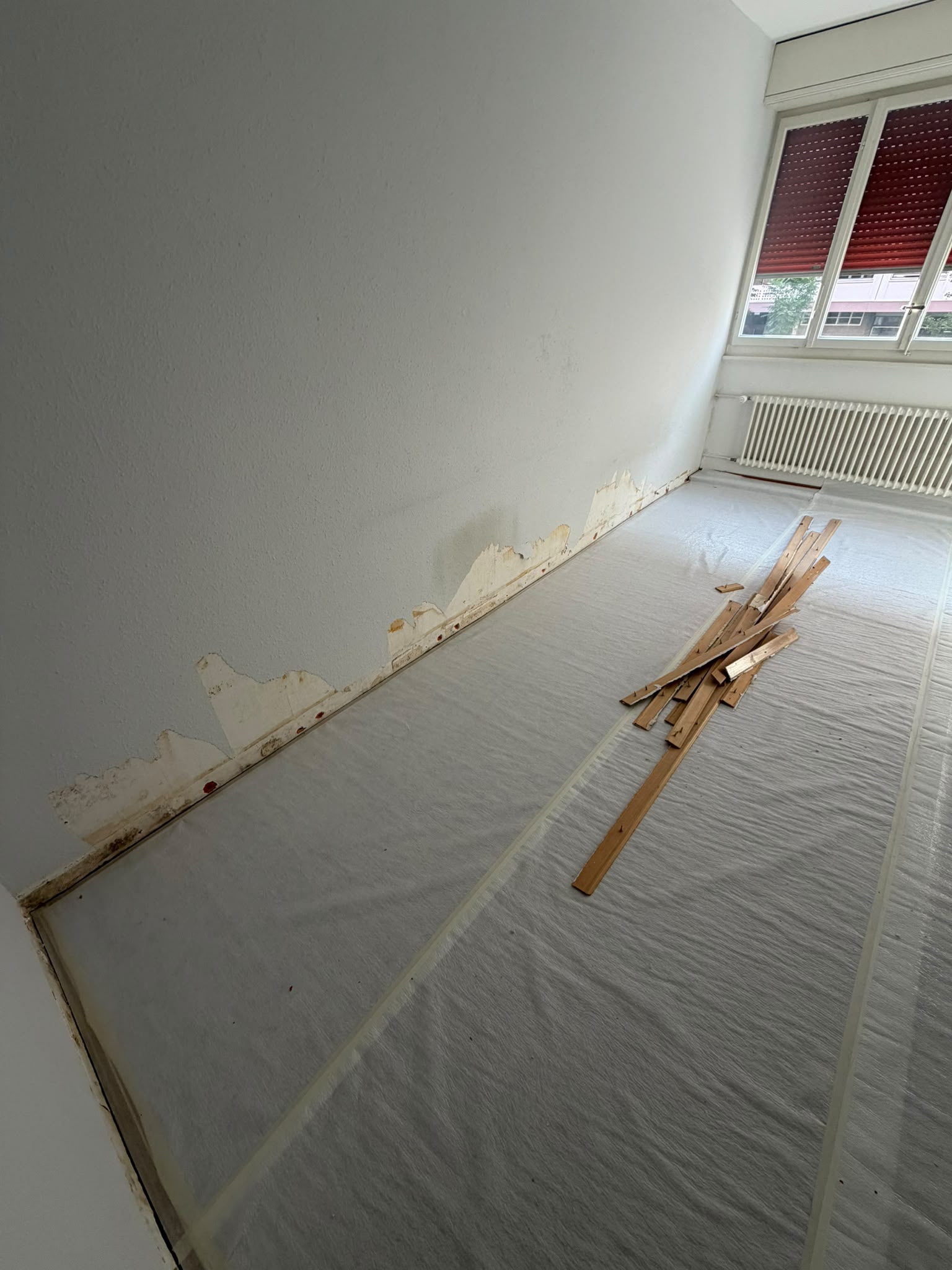 Avant : paroi abîmée par l’humidité en pied de mur, plinthes déposées, sol protégé avant réparation et peinture