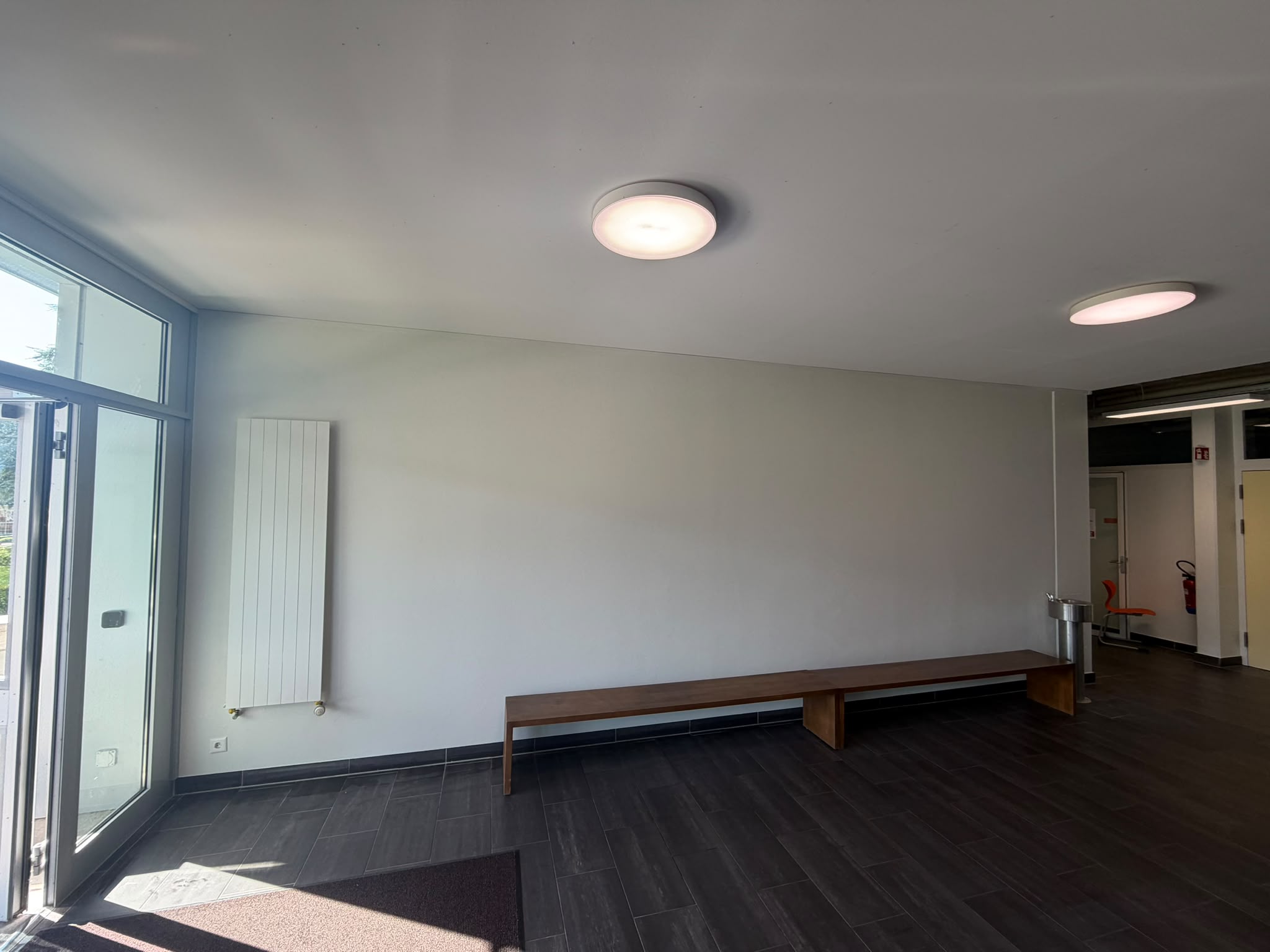 Après : le même mur lissé et peint en gris clair, plafond blanc, local commun avec banc en bois