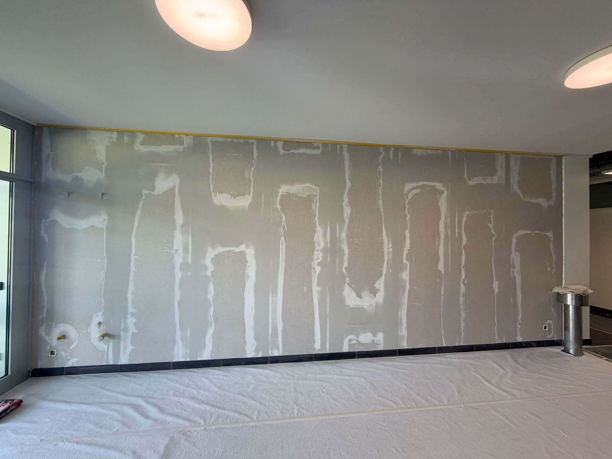 Avant : grand mur en plaques de plâtre avec bandes et enduit de rebouchage dans un local, prêt pour la préparation et la peinture