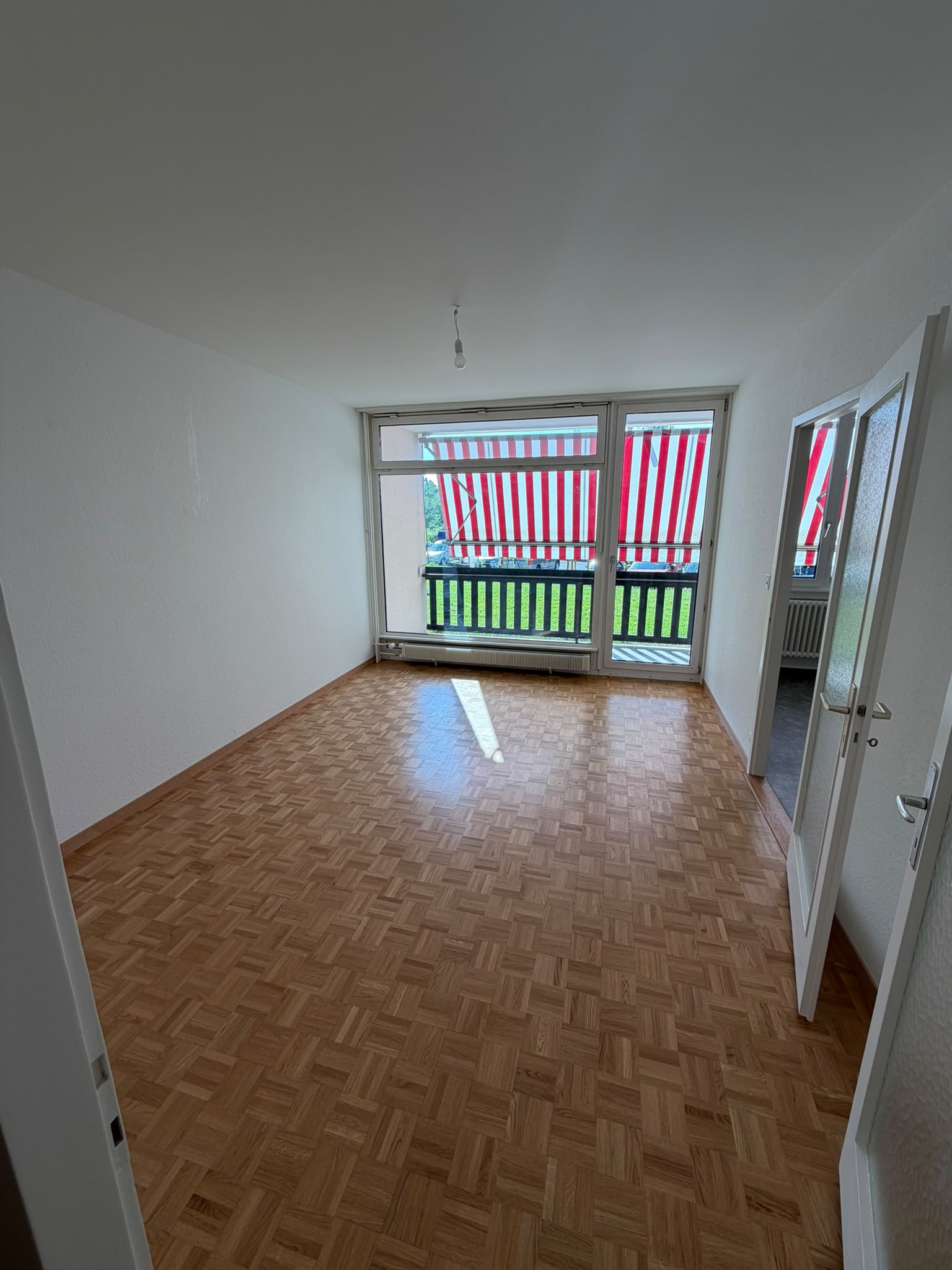Séjour aux murs blancs fraîchement peints, grande baie vitrée et parquet mosaïque
